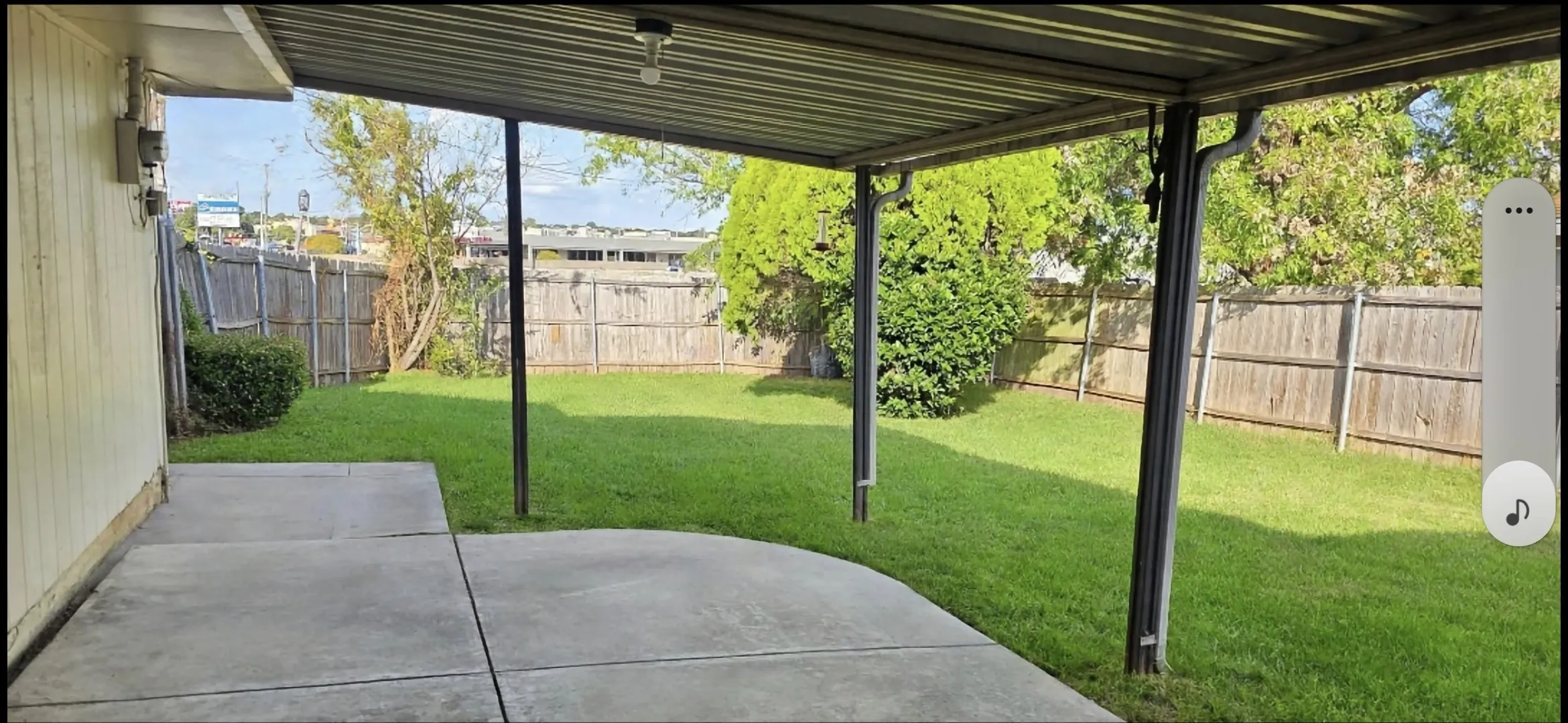 Expansive backyard featuring a covered patio, concrete surface, and wood privacy fencing