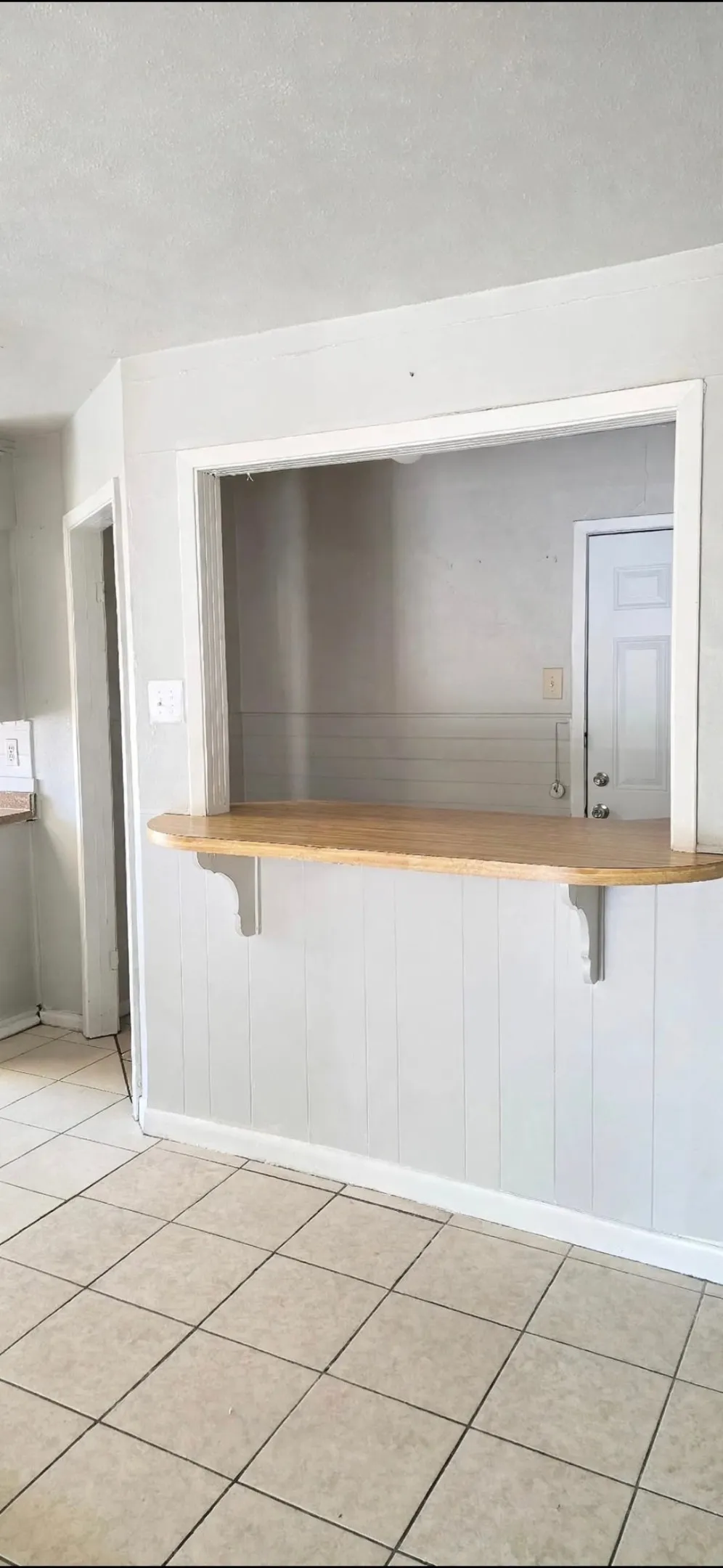 Breakfast bar with wood-finish countertop, supported by white brackets, ceramic tile flooring, and white paneled wainscoting