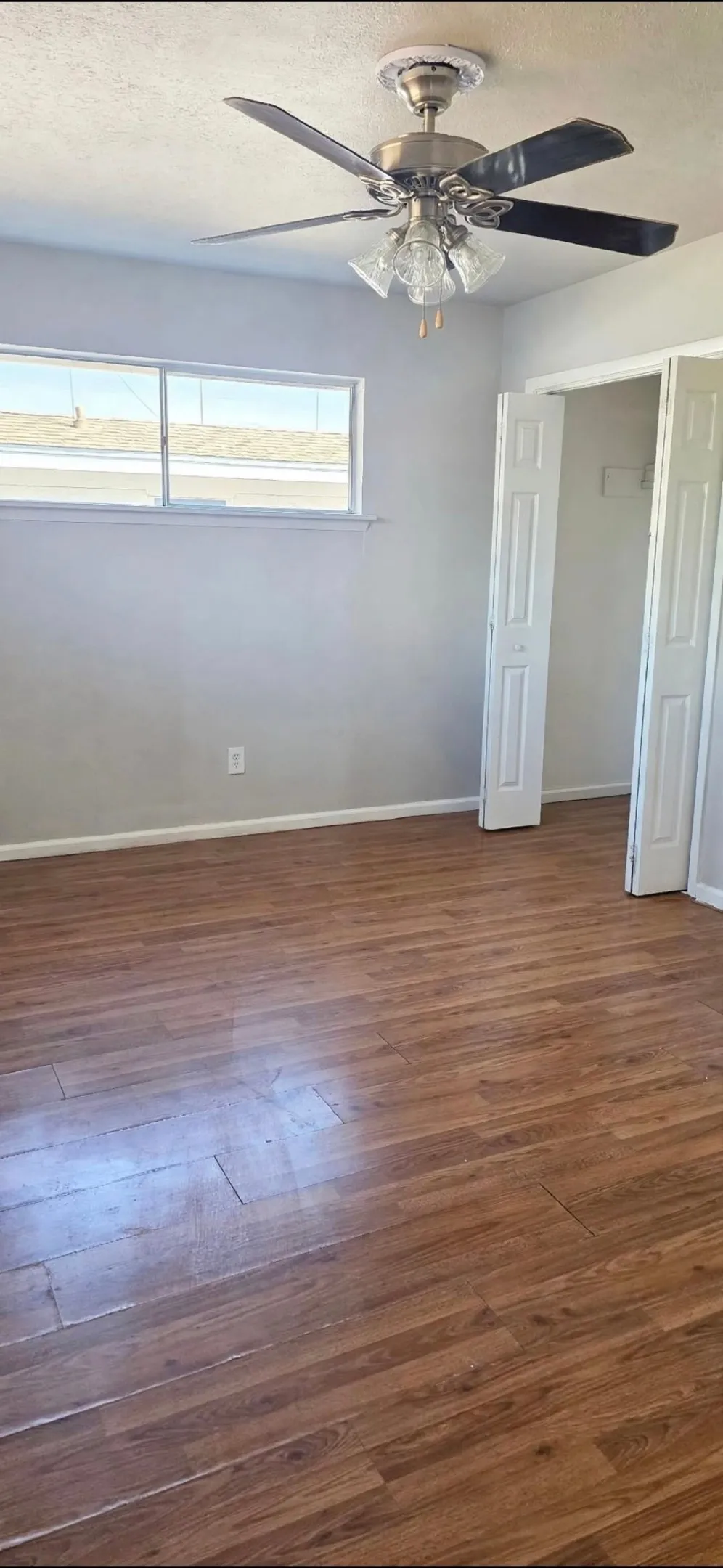 Primary Bedroom-pic 2- wood-finish flooring, ceiling fan with integrated lighting, horizontal window, and bifold closet doors
