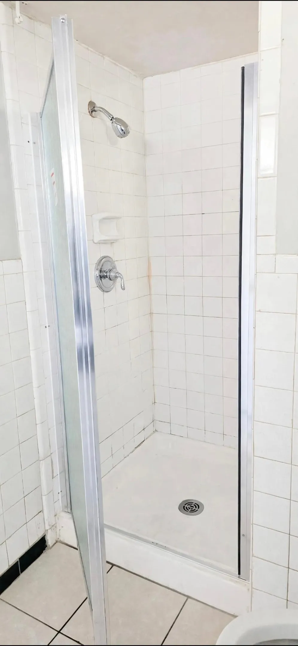 Walk-in shower with white tile surround, chrome showerhead, and single-handle mixing valve