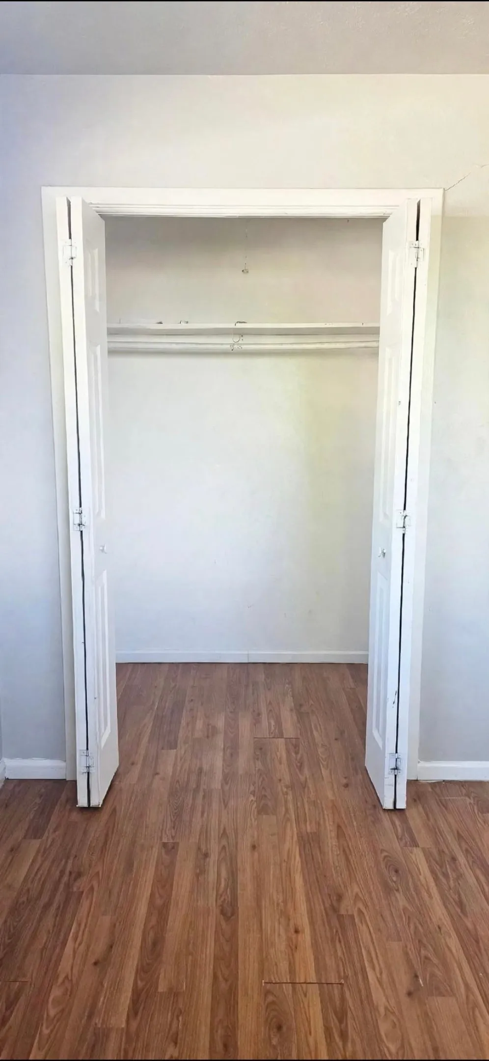 Wood-finish flooring with white baseboards and bi-fold closet doors