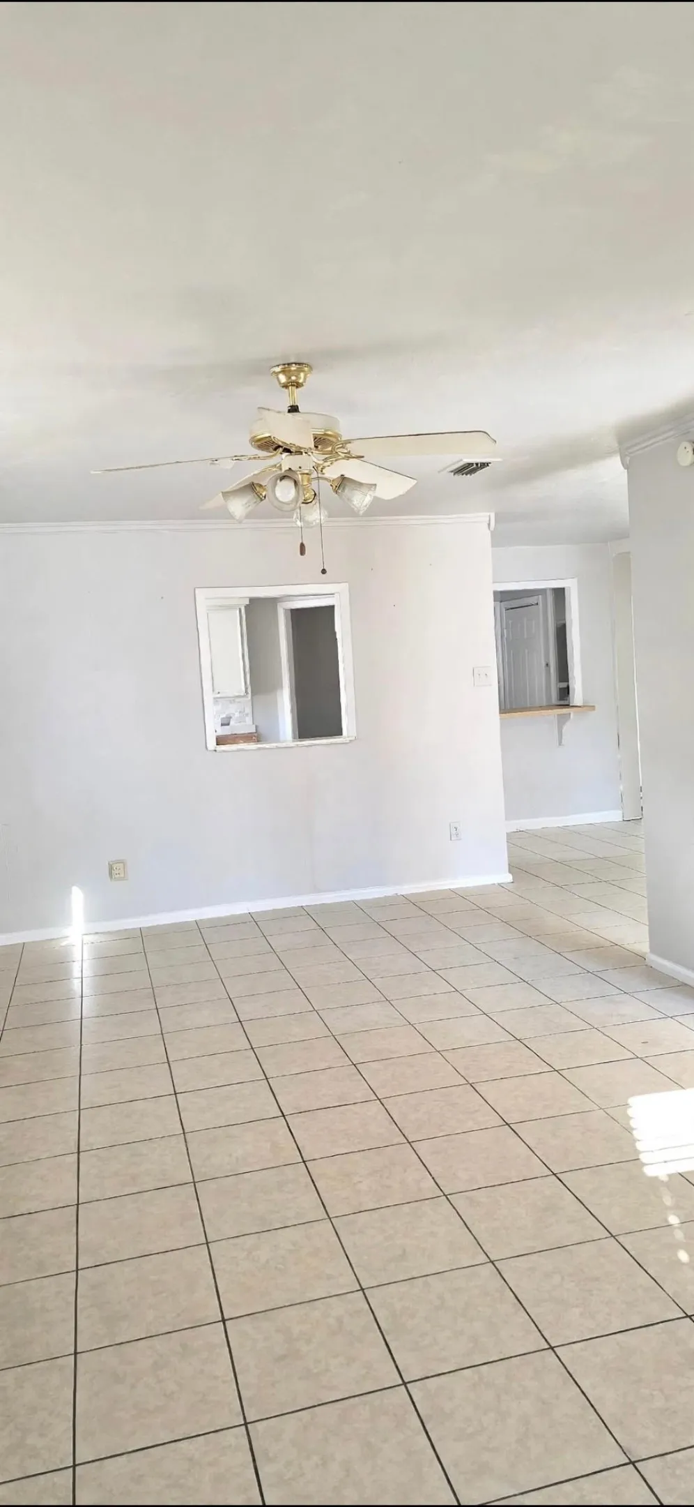 Tile flooring throughout with a ceiling fan light fixture and pass-through window