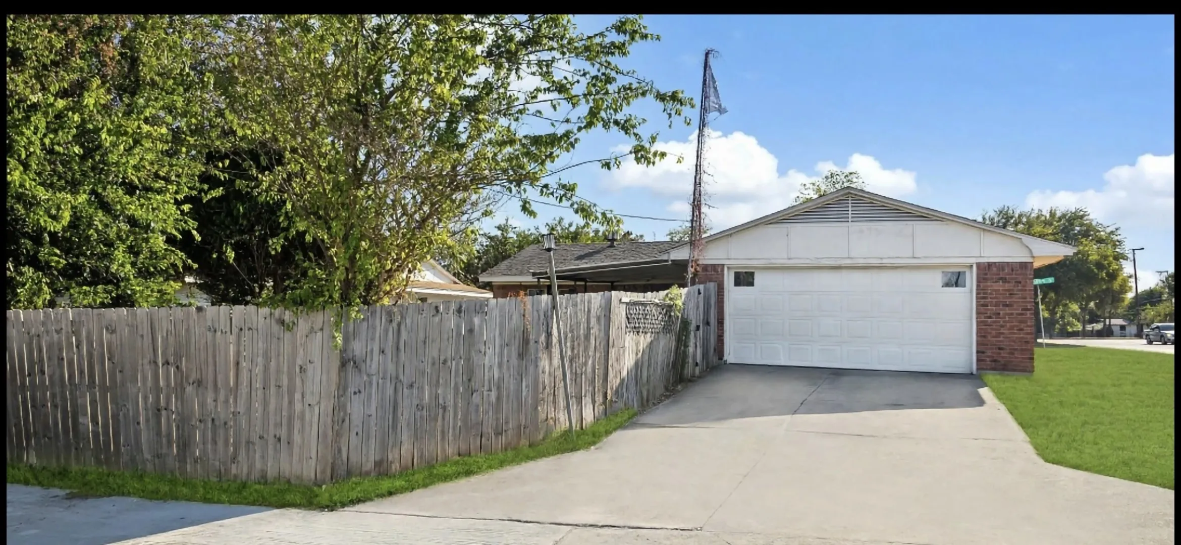 Brick exterior, attached garage, concrete driveway, wood privacy fence, and a manicured lawn