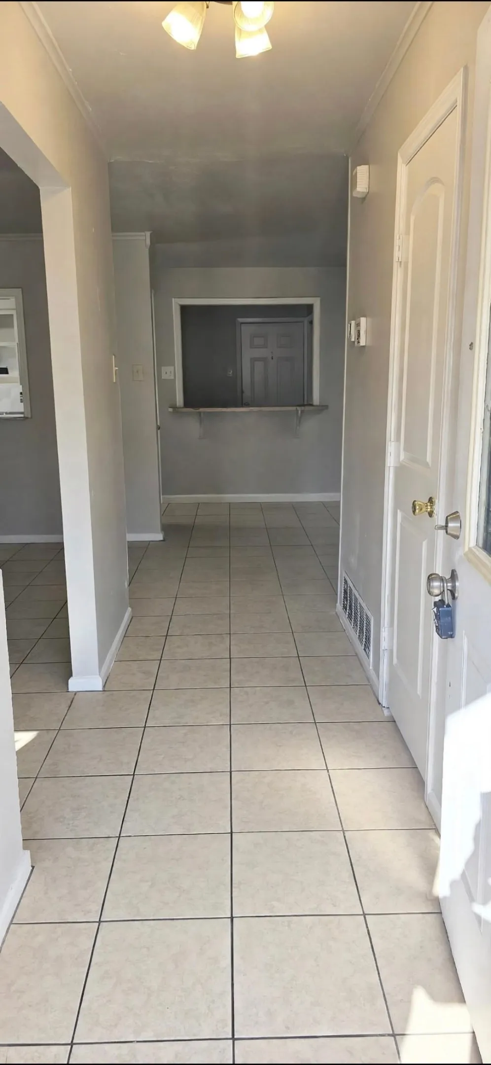 Tiled flooring entryway with a ceiling-mounted light fixture, leading to an interior doorway with a pass-through window