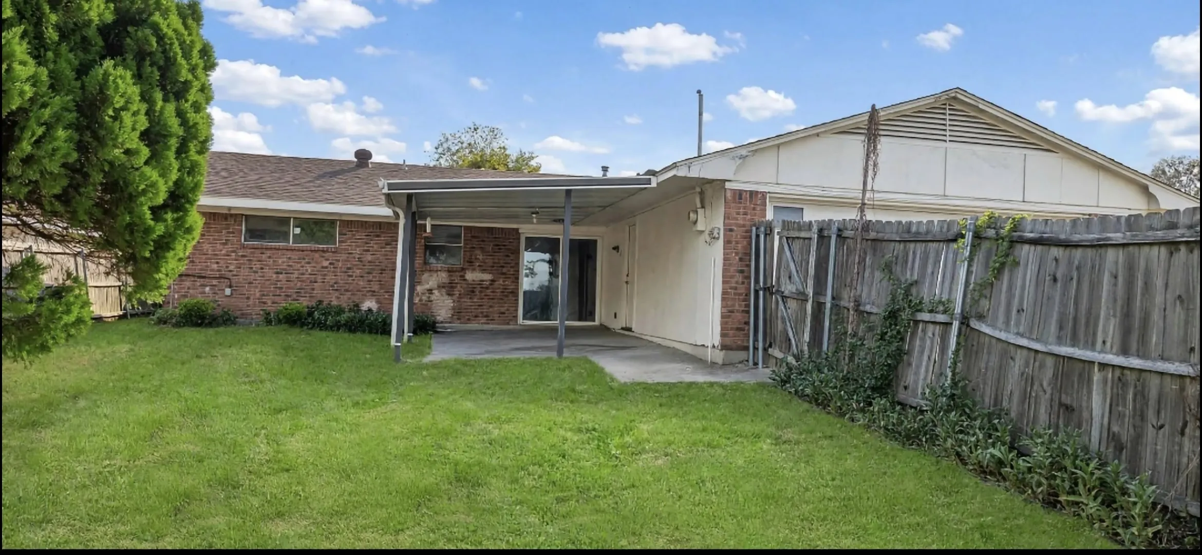 Expansive backyard featuring a covered patio, brick exterior, and a wood privacy fence