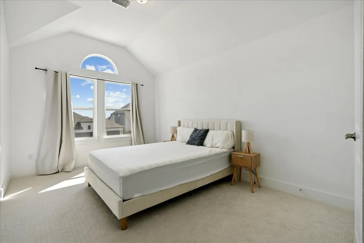 Vaulted ceiling with an arched window above two rectangular windows, light-toned carpeting, and a white interior door