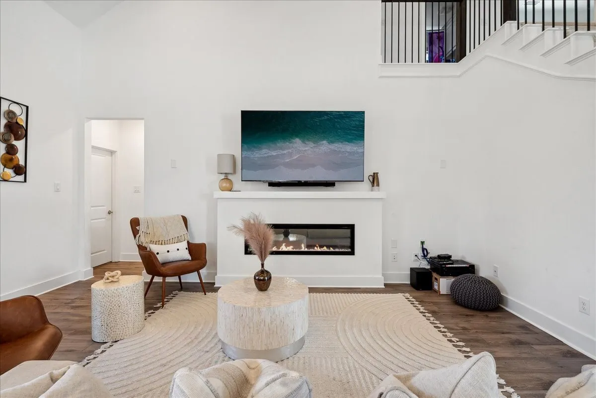 Open-concept living area featuring vaulted ceilings, wood-finish flooring, a built-in linear fireplace, and a staircase with metal balusters