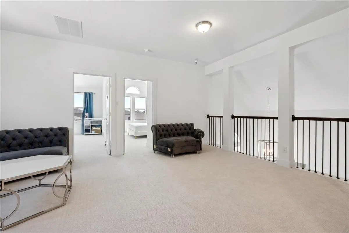 Spacious second-level landing with carpet flooring, white walls, and dark iron balusters