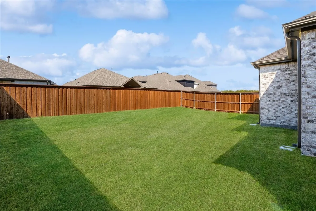 Expansive backyard featuring a lush lawn, privacy fencing, and brick exterior