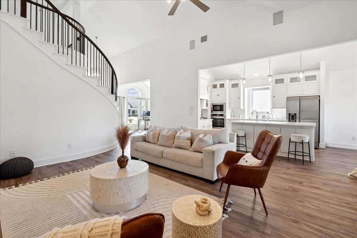Soaring vaulted ceiling, curved staircase with wrought iron balusters, wood-finish flooring, and a kitchen with white cabinetry and stainless steel appliances