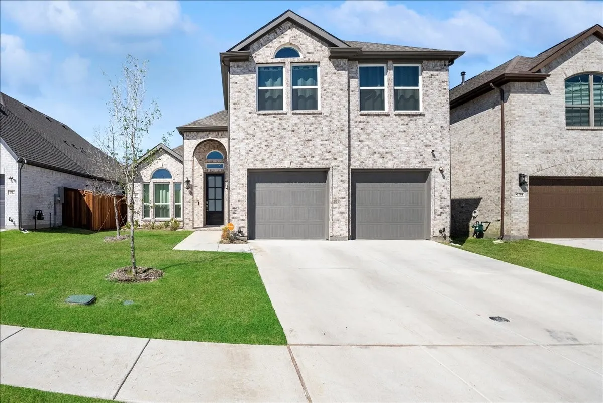 Brick facade with arched entryway, dual garage bays, concrete driveway, and front lawn