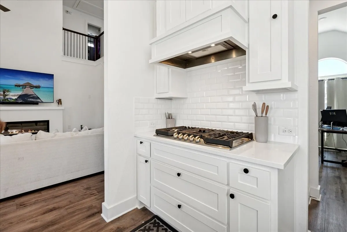 White shaker cabinetry, subway tile backsplash, white countertops, built-in gas range, and a built-in oven hood
