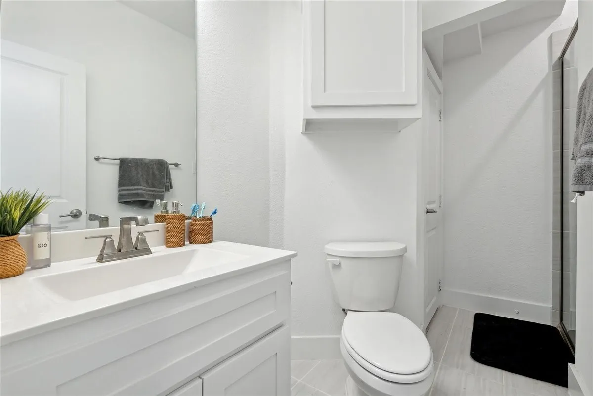 White vanity with integrated sink, brushed nickel faucet, wall-mounted mirror, and white toilet