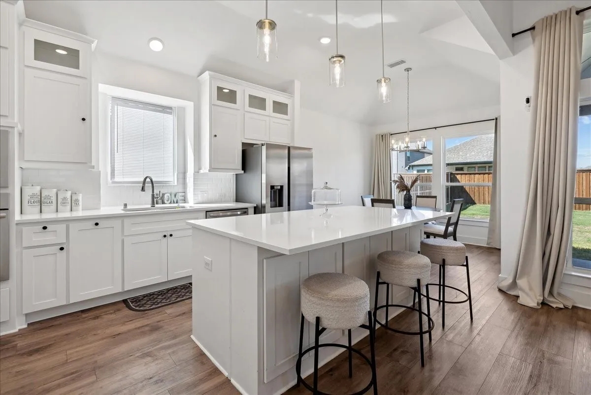 Kitchen featuring white cabinetry, a large center island with a white countertop, stainless steel appliances, wood-finish flooring, and pendant lighting