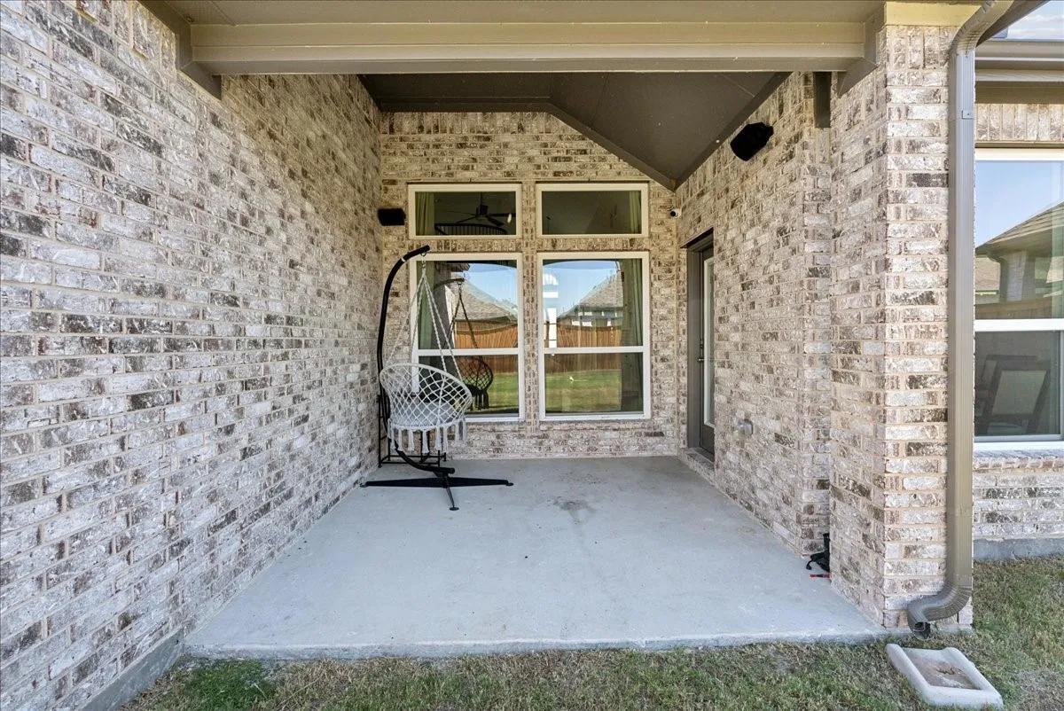 Covered concrete patio with brick exterior, multiple windows, and exterior door access