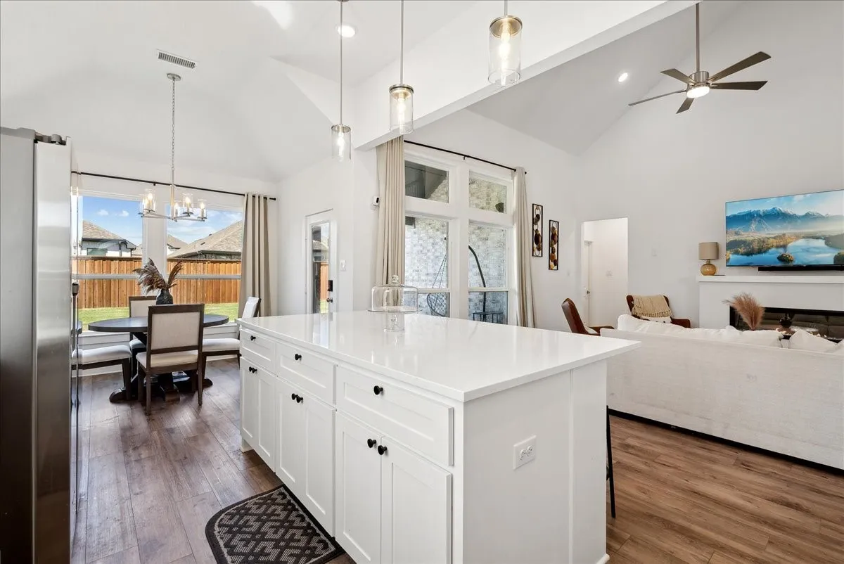 Vaulted ceilings, wood-finish flooring, white kitchen island with counter seating, stainless steel appliances, and a built-in fireplace
