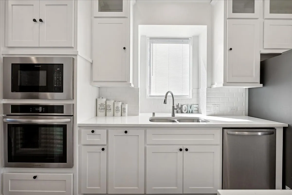Crisp white cabinetry, stainless steel appliances, a subway tile backsplash, and a double basin sink with a gooseneck faucet