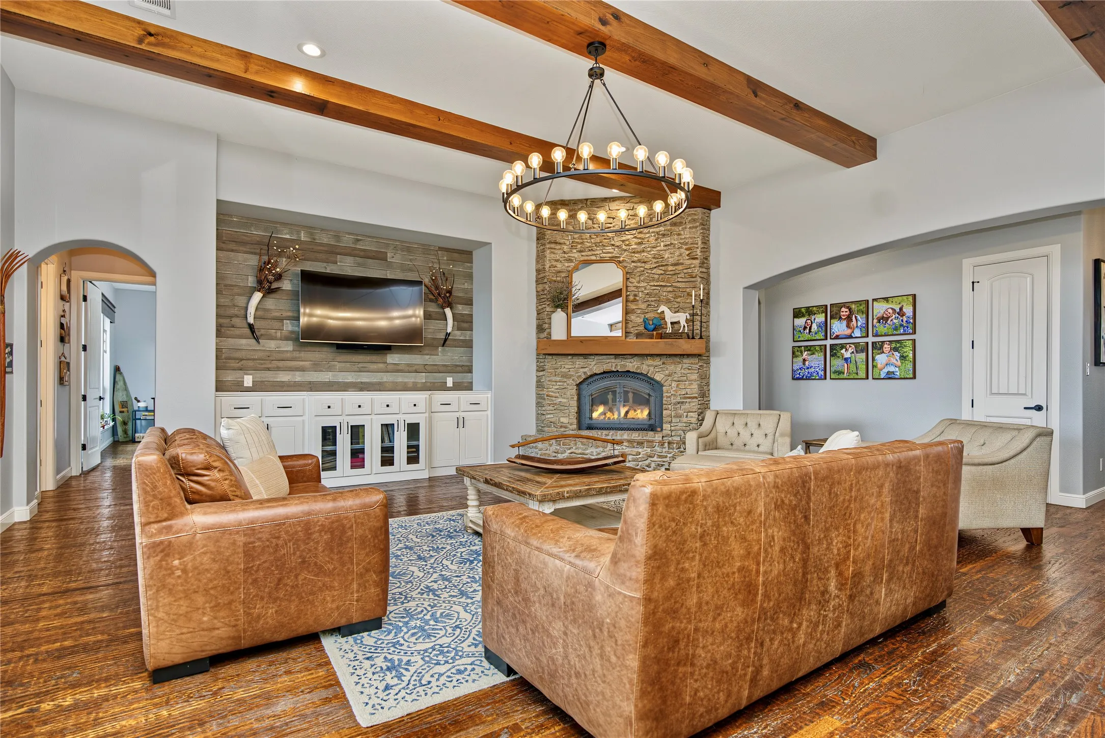 Exposed wood ceiling beams, stone-faced fireplace with hearth, wood-finish flooring, built-in media cabinetry, and an arched entryway