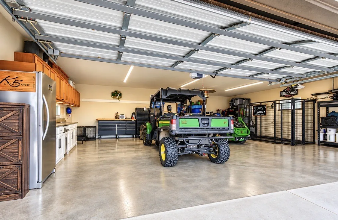 Expansive garage featuring polished concrete flooring, built-in cabinetry, stainless steel appliances, and task lighting