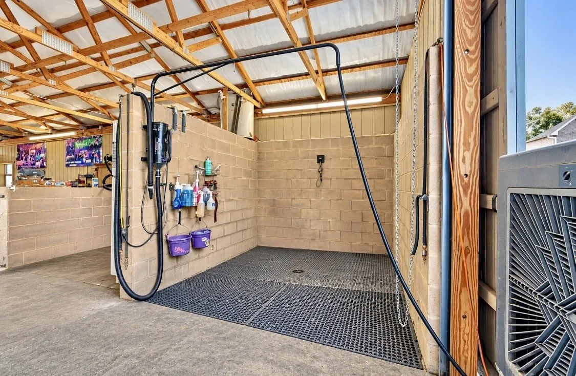 Open-air wash stall with concrete block walls, slatted rubber flooring, exposed wood beam ceiling, and overhead lighting