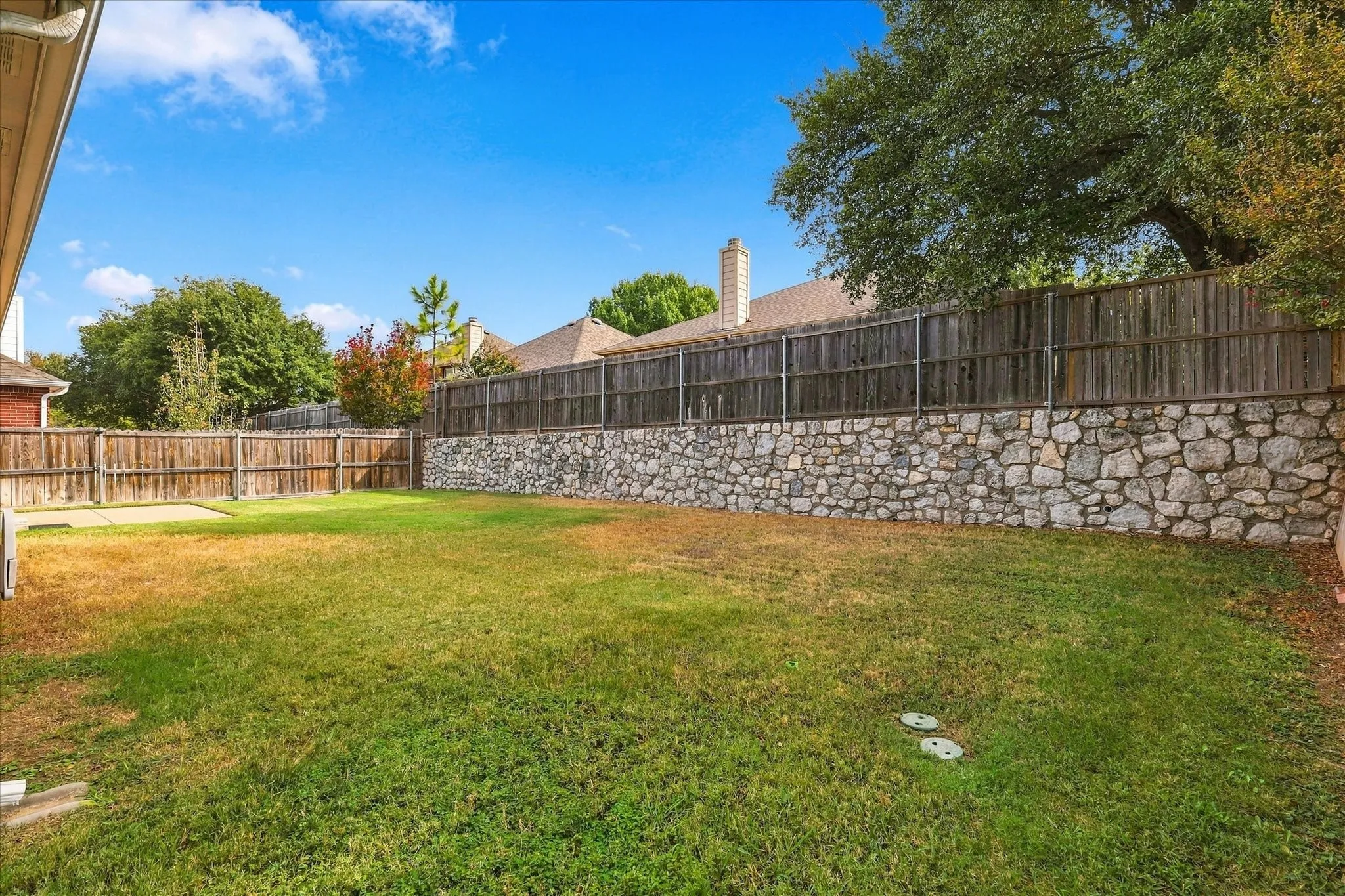A stone retaining wall topped with a wood fence provides added privacy from the rear neighbors, creating a more secluded backyard setting.