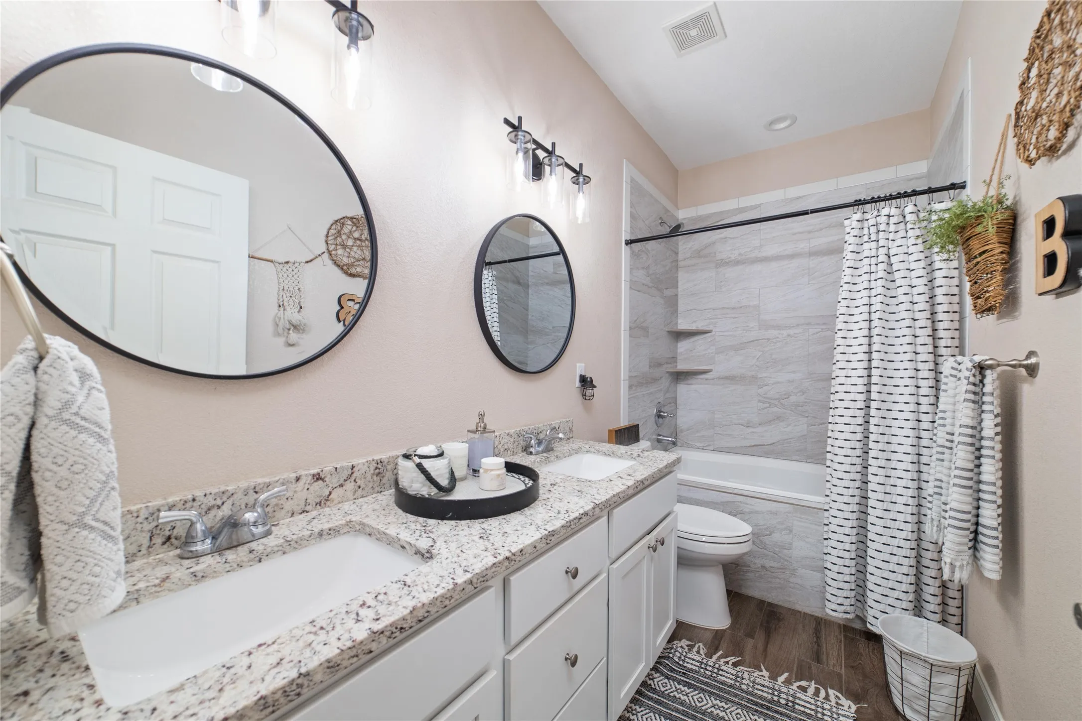 Full bathroom with dual vanity, shower / bathtub combination with curtain, toilet, and hardwood / wood-style flooring