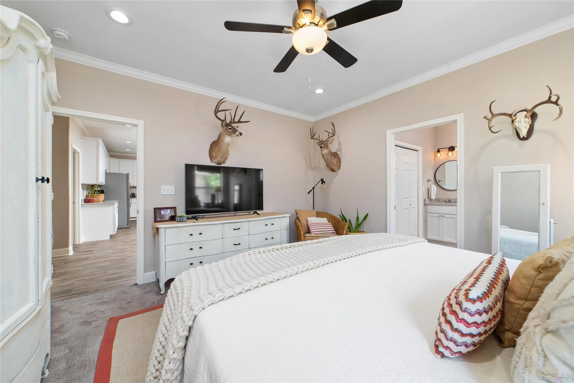 Bedroom featuring light carpet, ceiling fan, ornamental molding, ensuite bathroom, and stainless steel refrigerator