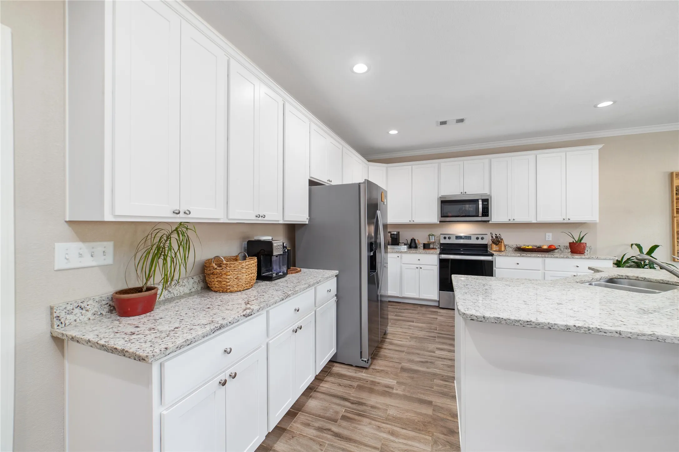 Kitchen with appliances with stainless steel finishes, light stone countertops, white cabinets, light hardwood / wood-style flooring, and sink