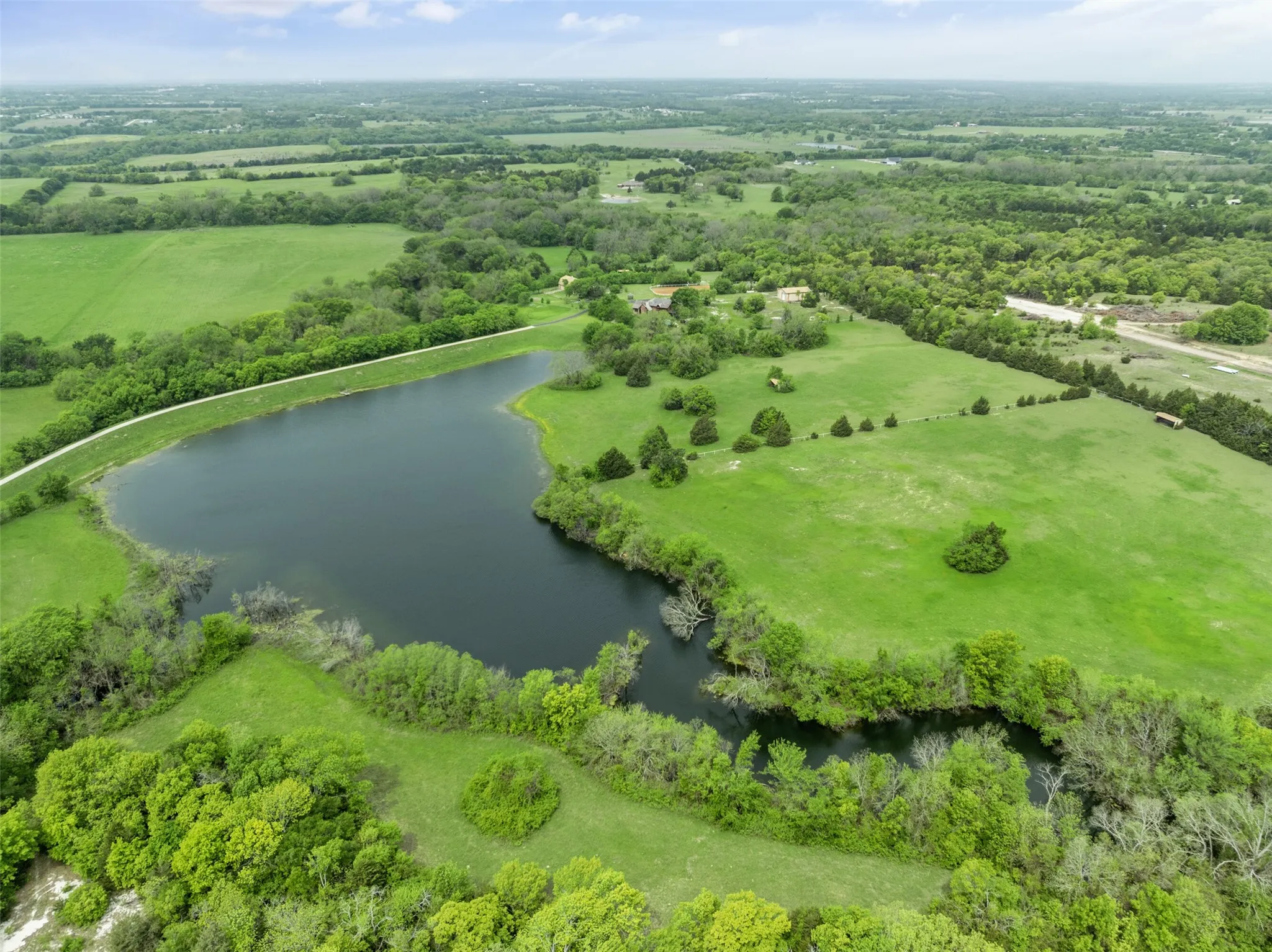 Expansive landscape featuring an irregular-shaped pond, abundant greenery, and scattered trees