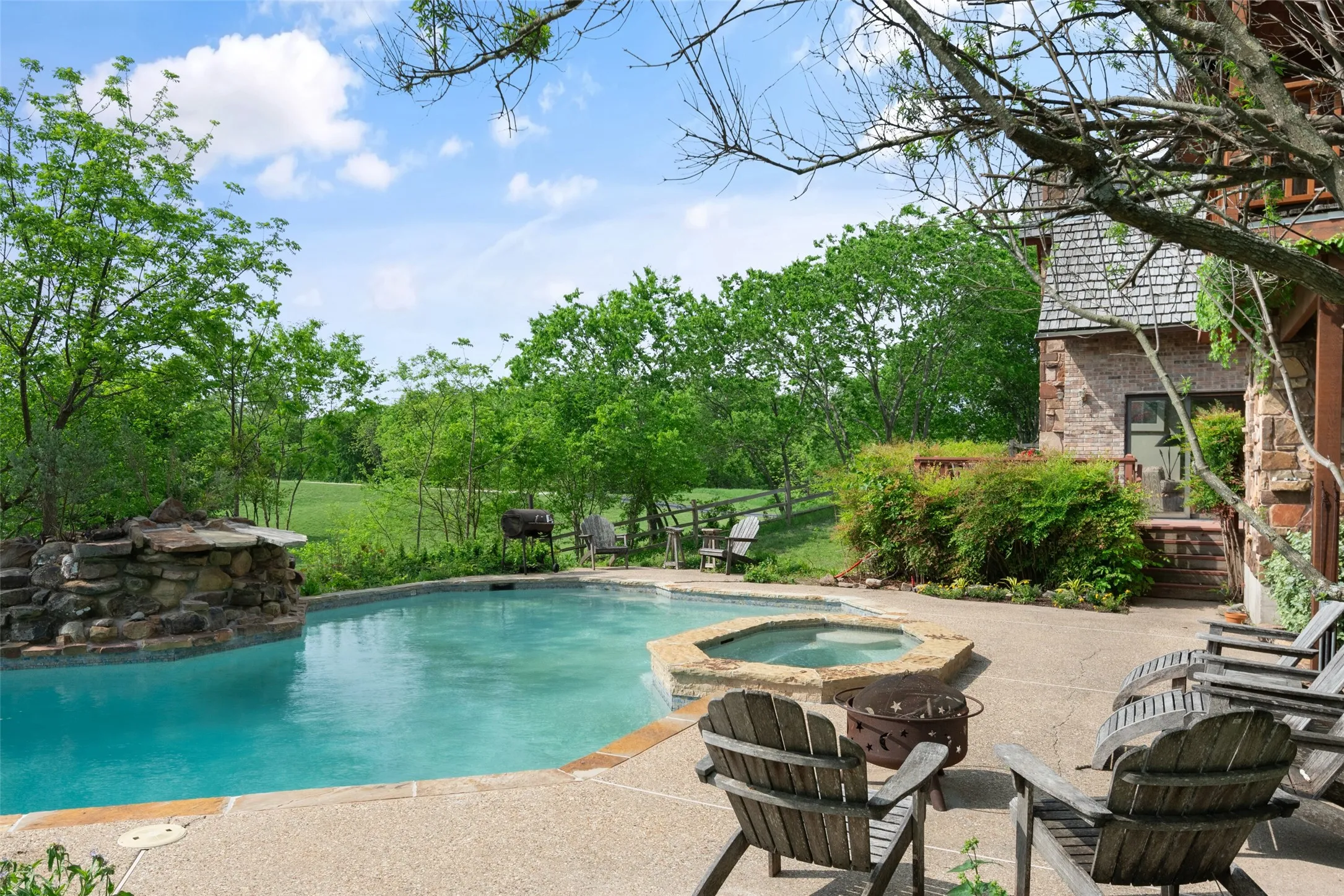 In-ground swimming pool with an integrated spa and rock waterfall feature, surrounded by concrete decking