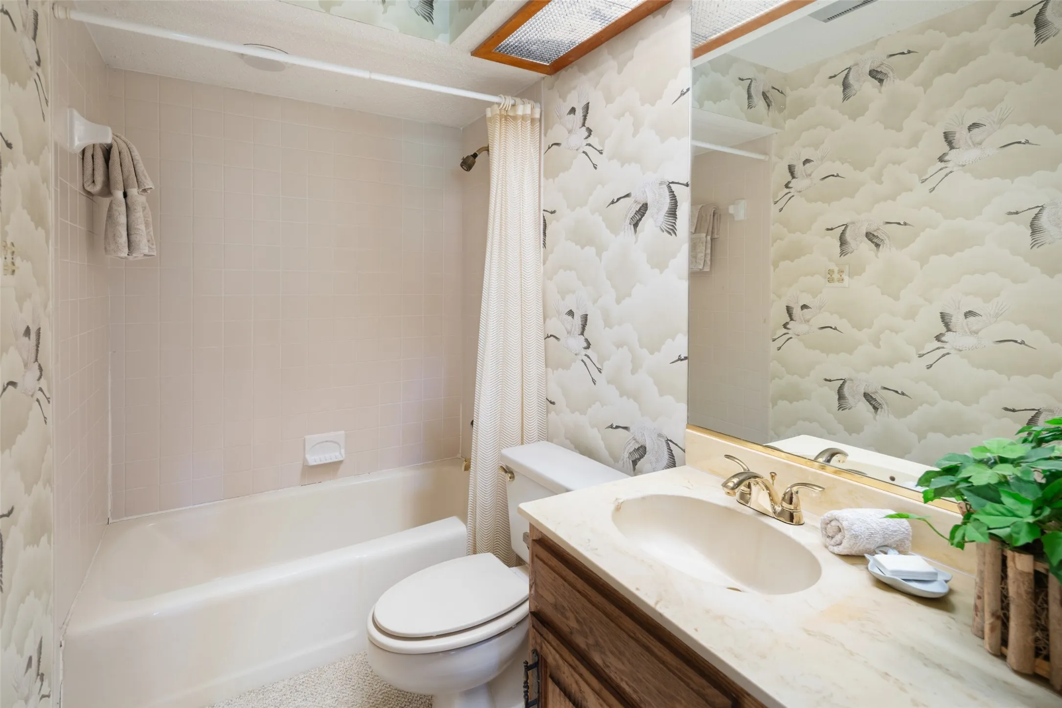 Bathroom featuring a shower-tub combination, a vanity with an integrated sink, a large mirror, and patterned wall covering