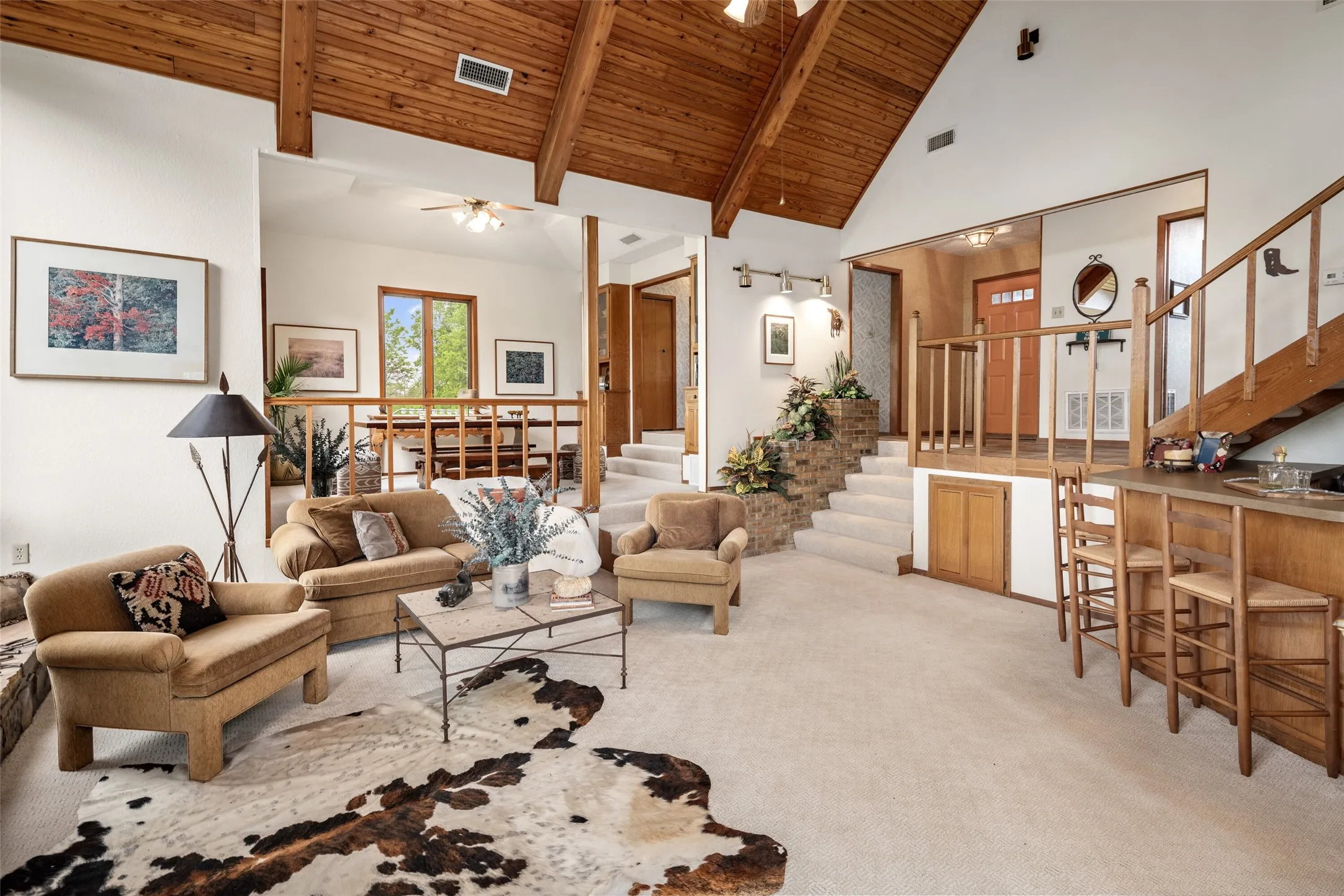 Vaulted wood-paneled ceiling with exposed beams, built-in bar with wood cabinetry, carpeted staircase with wood railing, stone-clad planter, and wood-finish door