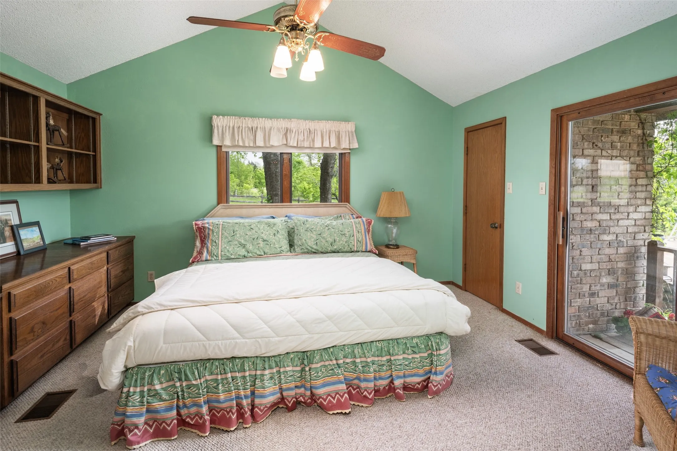 Vaulted ceiling with a ceiling fan, built-in wooden shelving, a window with wooden trim, and a glass sliding door