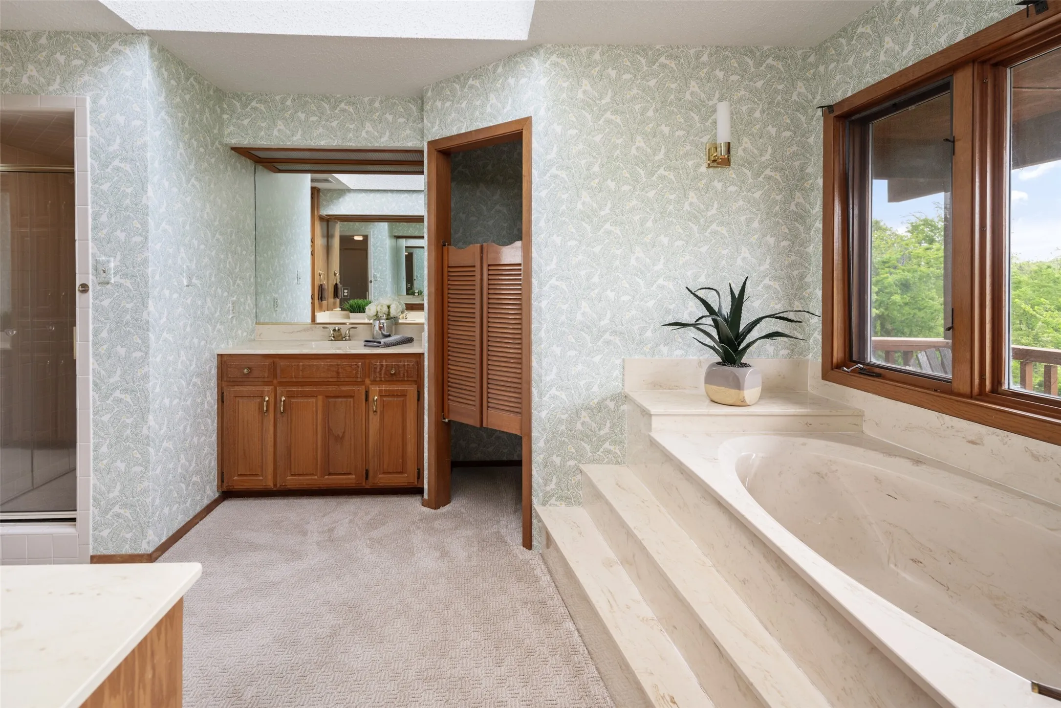 Built-in bathtub with tiered surround, wood-framed window, wood vanity with integrated sink, and mirrored wall