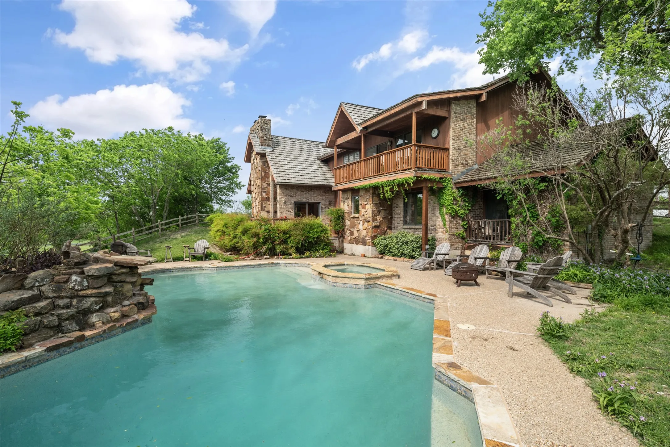 Stone and wood-sided exterior with a multi-level balcony, a swimming pool, and an integrated spa