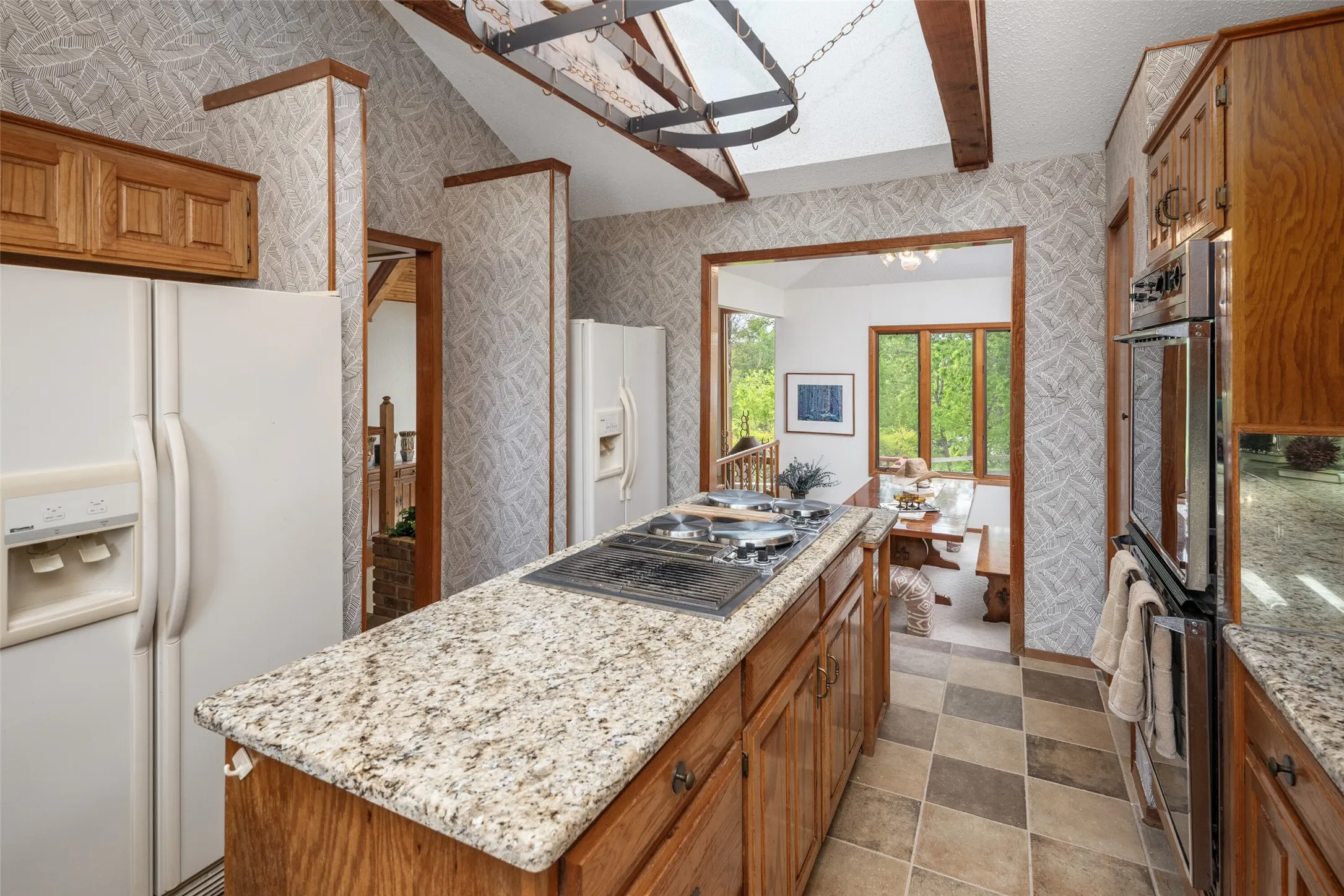 Kitchen featuring wood cabinetry, granite-finish countertops, a double oven, a center island with cooktop, and checkerboard floor tiling
