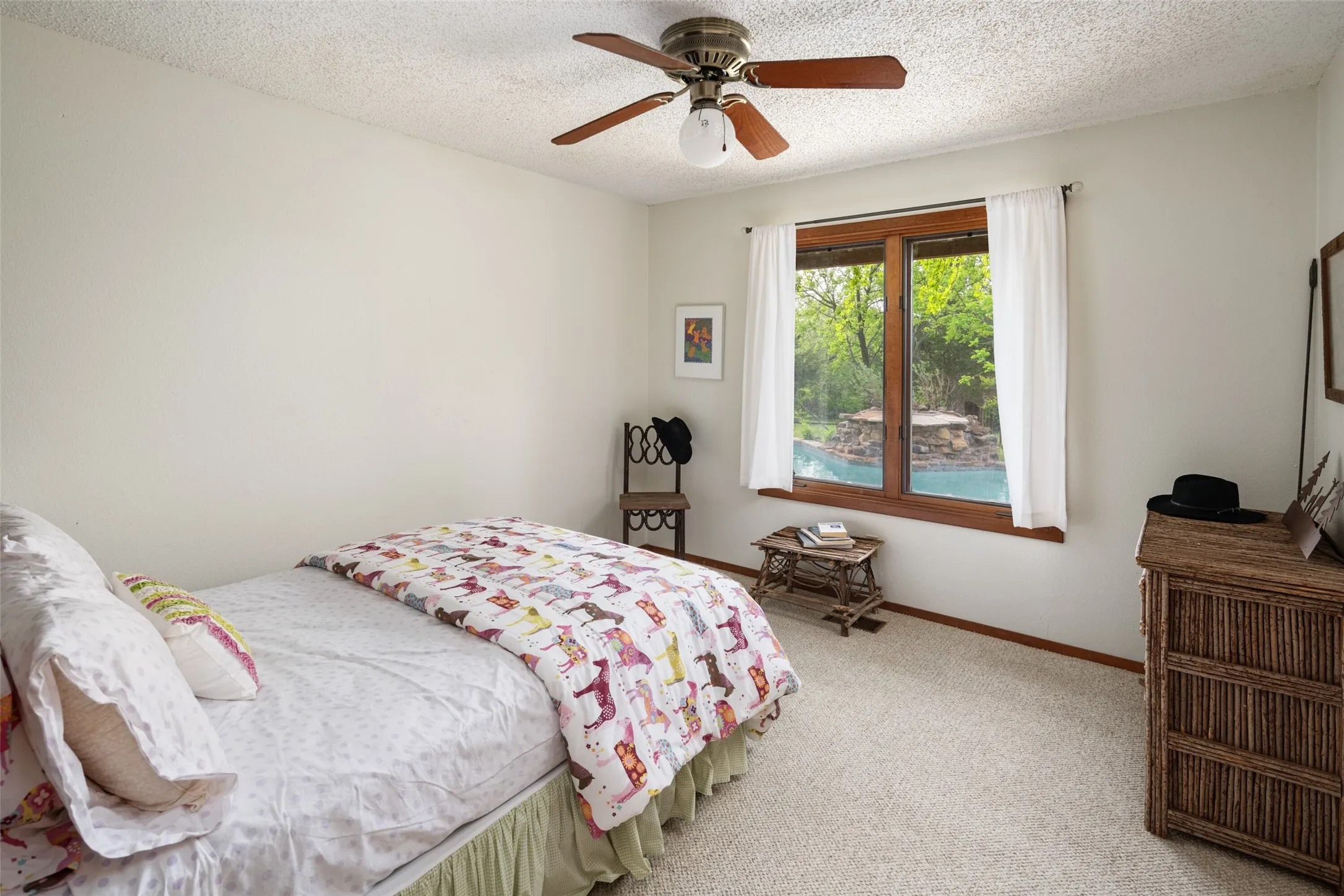 Light-colored carpeting, a ceiling fan with integrated lighting, and a wood-framed window overlooking an outdoor pool