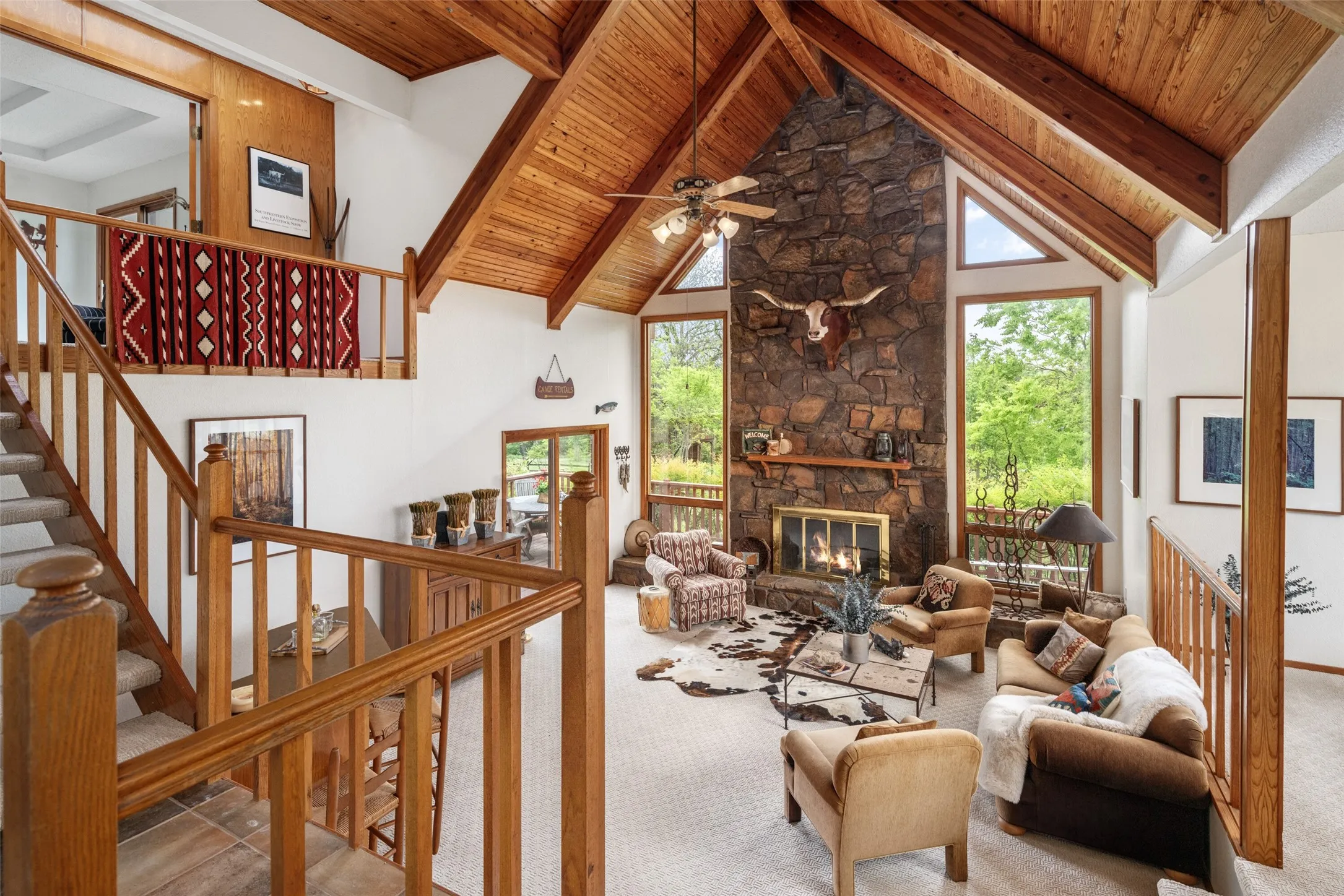 Vaulted wood-paneled ceilings, a stone-clad fireplace, and an open-tread staircase with wood railings
