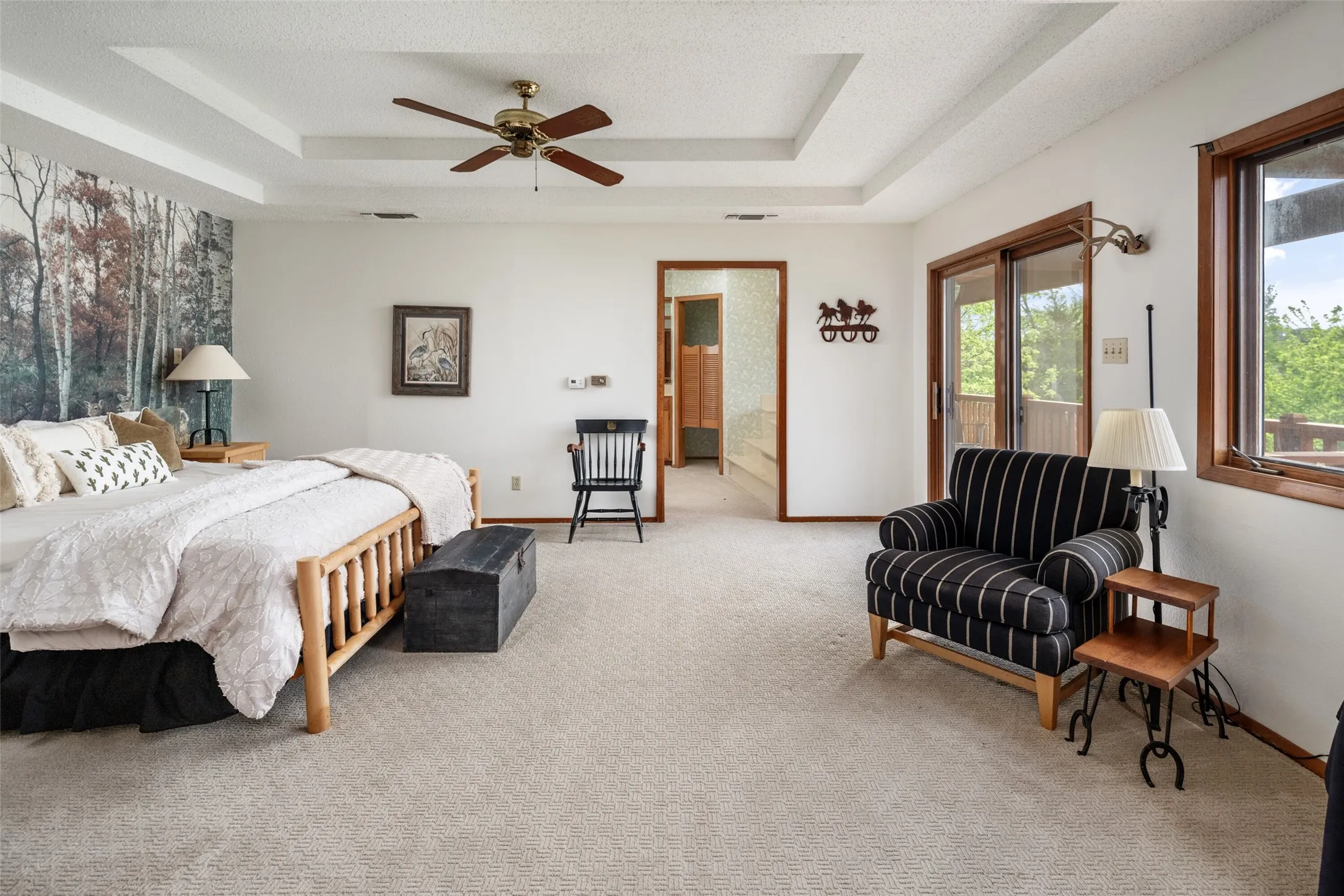 Tray ceiling with a ceiling fan, light-toned carpeting, wood-trimmed windows, and a sliding glass door providing exterior access