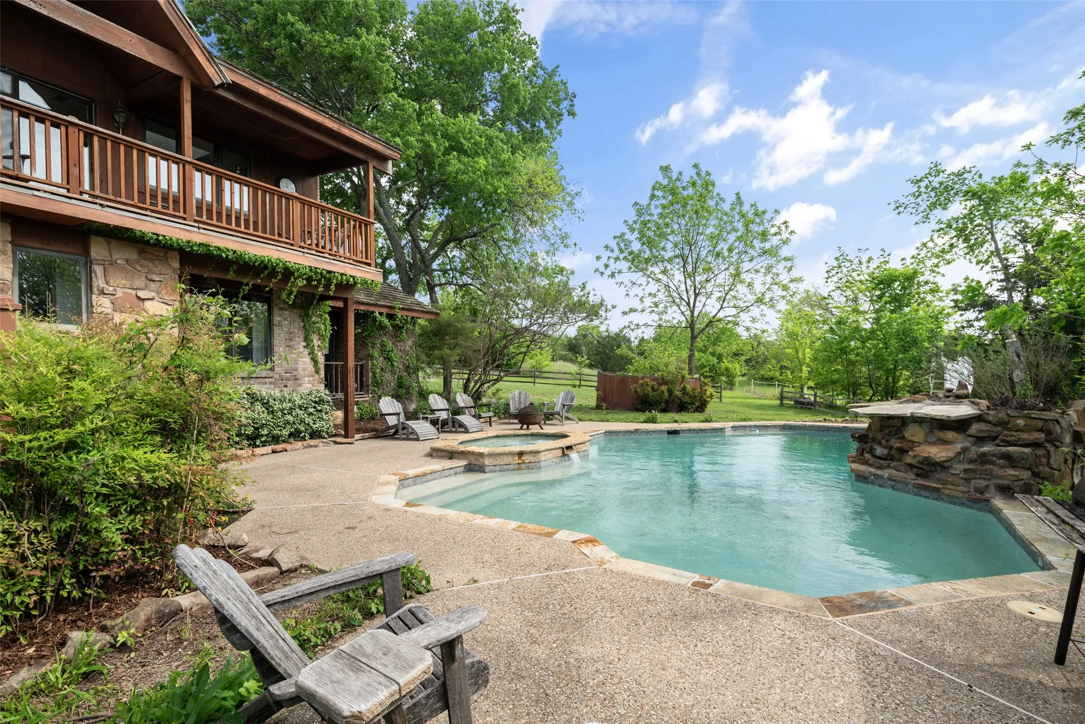 Stone exterior with upper-level balcony, ground-level patio, swimming pool, and integrated hot tub with stone surround