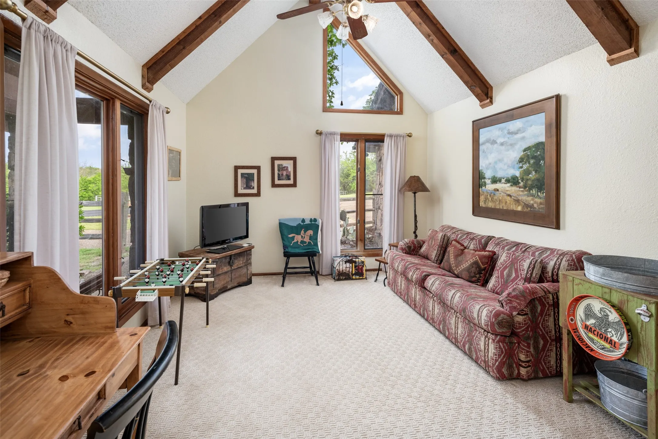 Vaulted ceiling with exposed wood beams, ceiling fan, and a triangular transom window