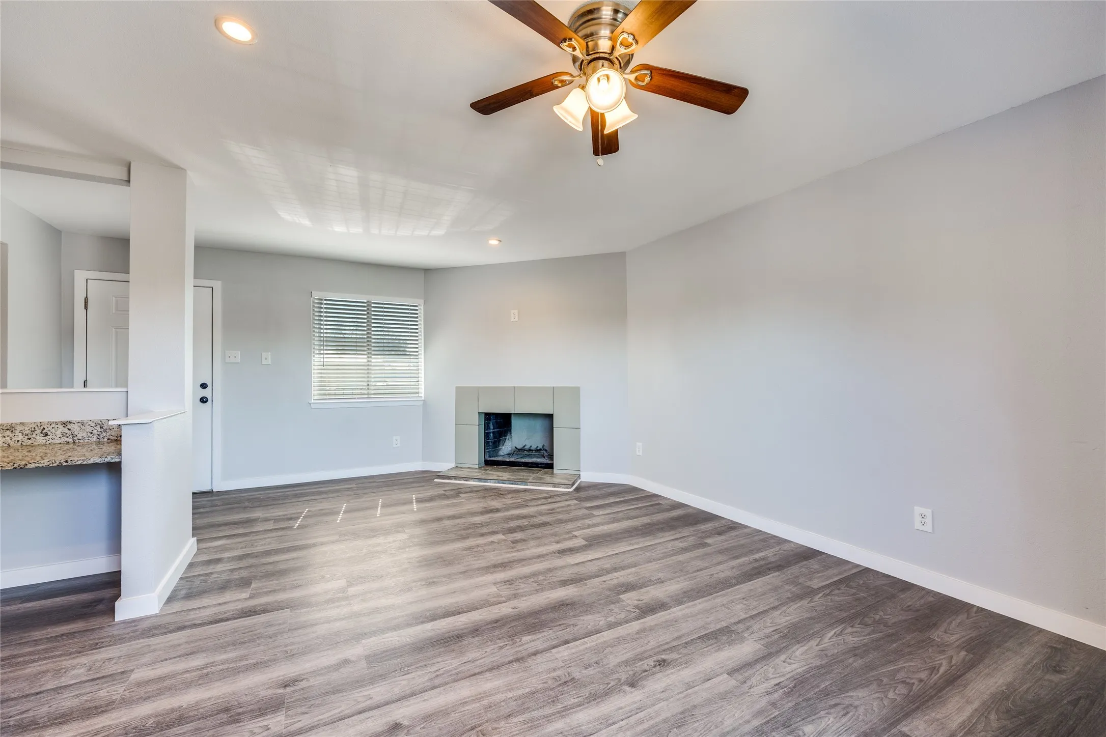 Spacious living area featuring wood-finish flooring, a ceiling fan with integrated lighting, recessed lighting, and a tile-surround fireplace