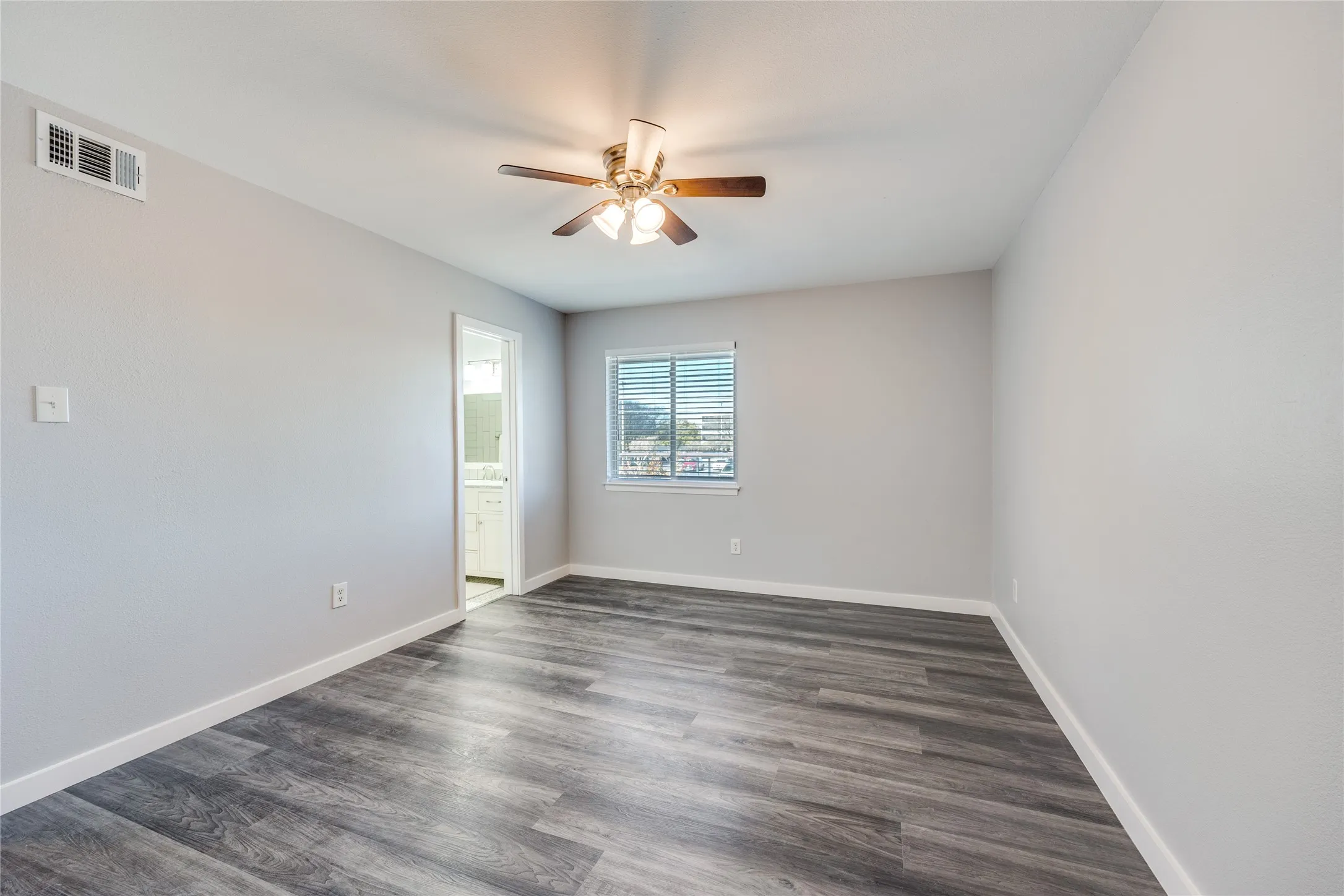 Wood-finish flooring, light gray wall tones, ceiling fan with integrated lighting, and a window with horizontal blinds