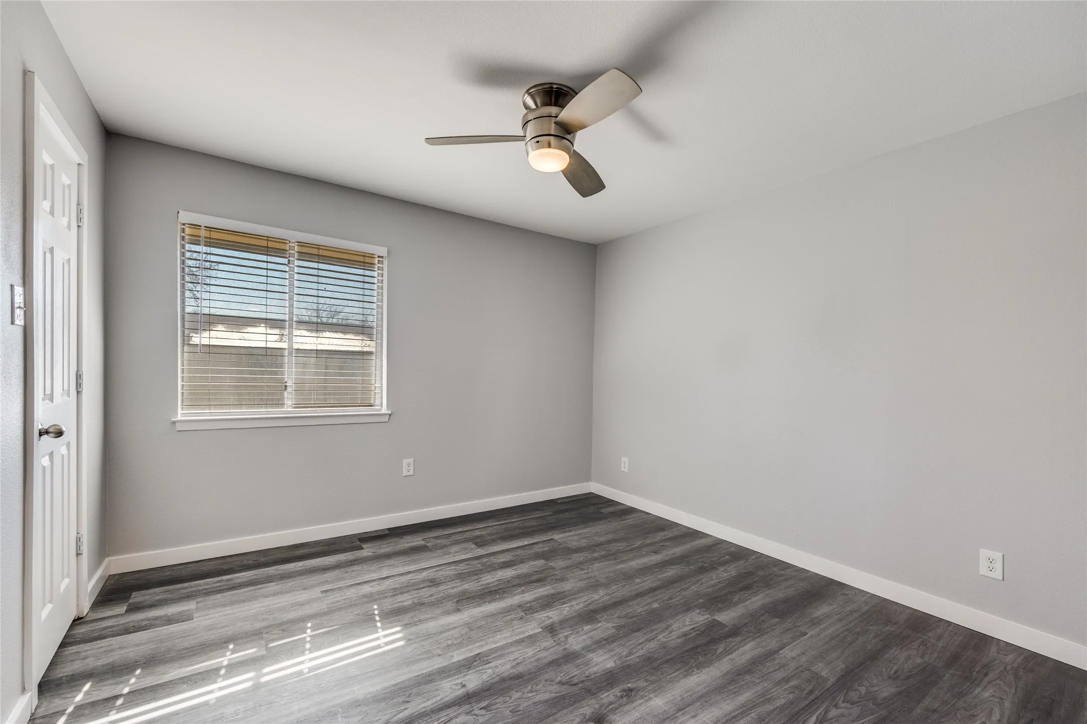 Wood-finish flooring with light gray walls, a window with blinds, and a ceiling fan