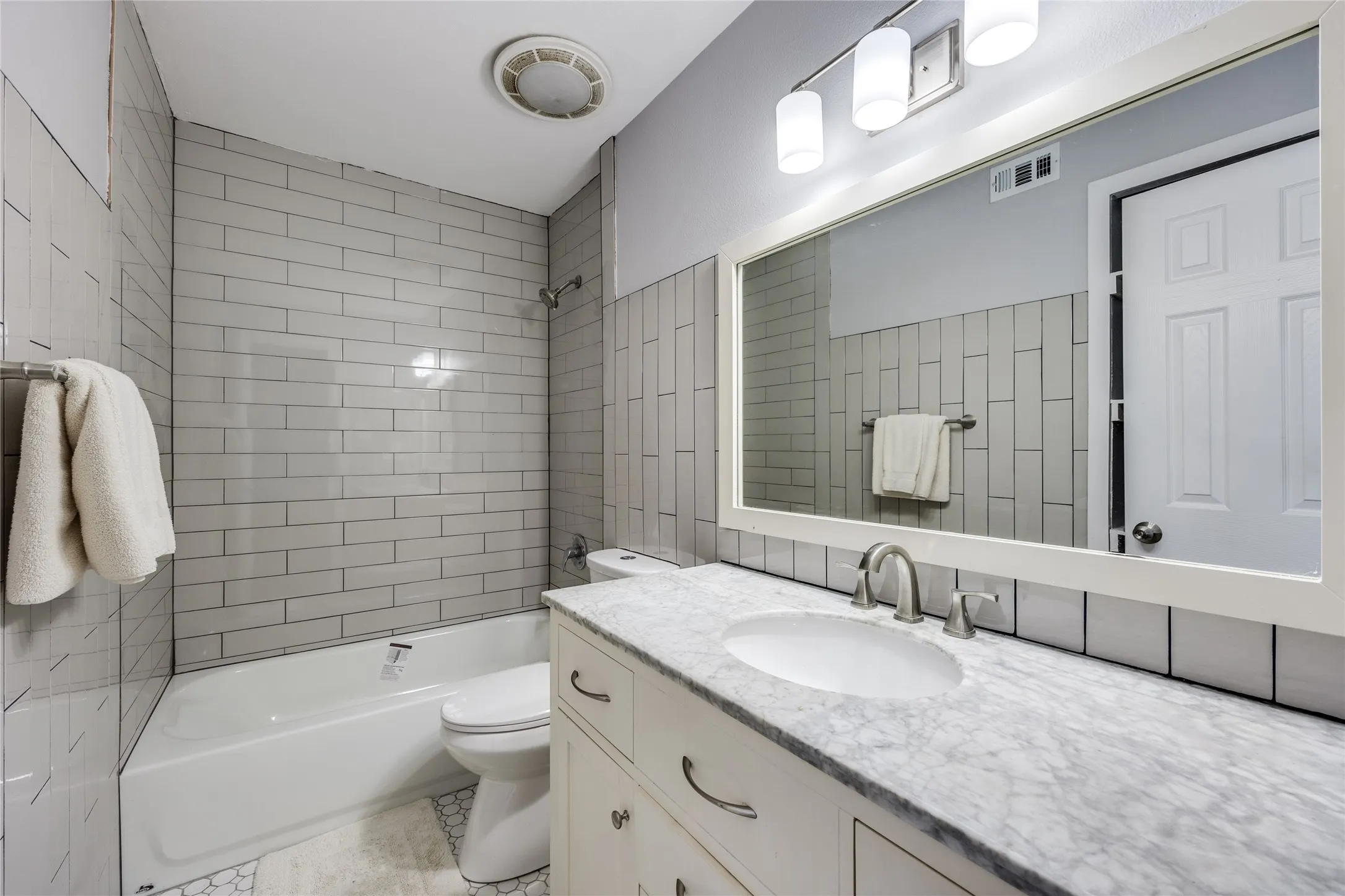 White vanity with a stone countertop and undermount sink, accented by a large framed mirror and three-light fixture