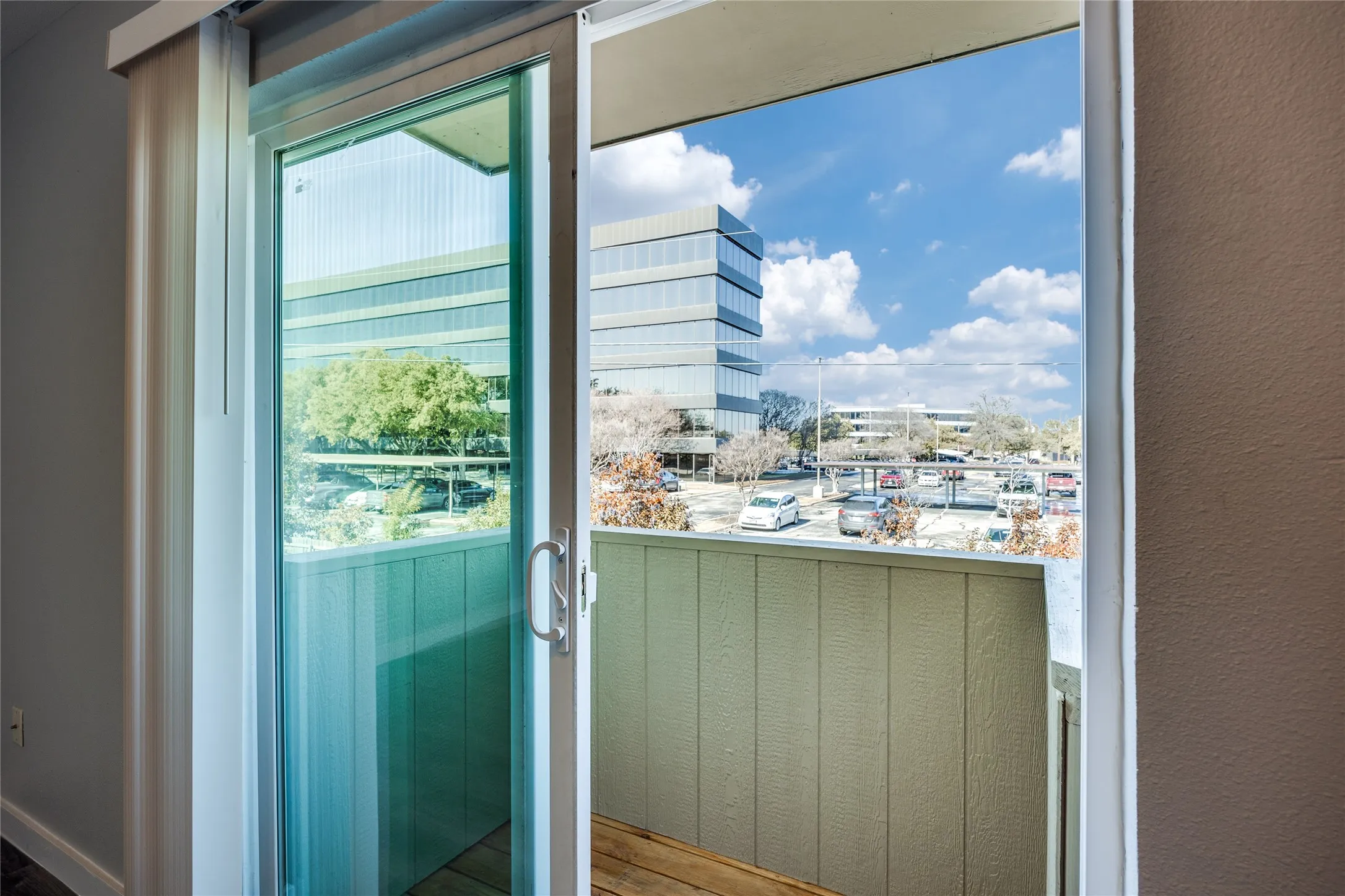 Sliding glass door leading to a private outdoor balcony with a wood-finish floor and paneling