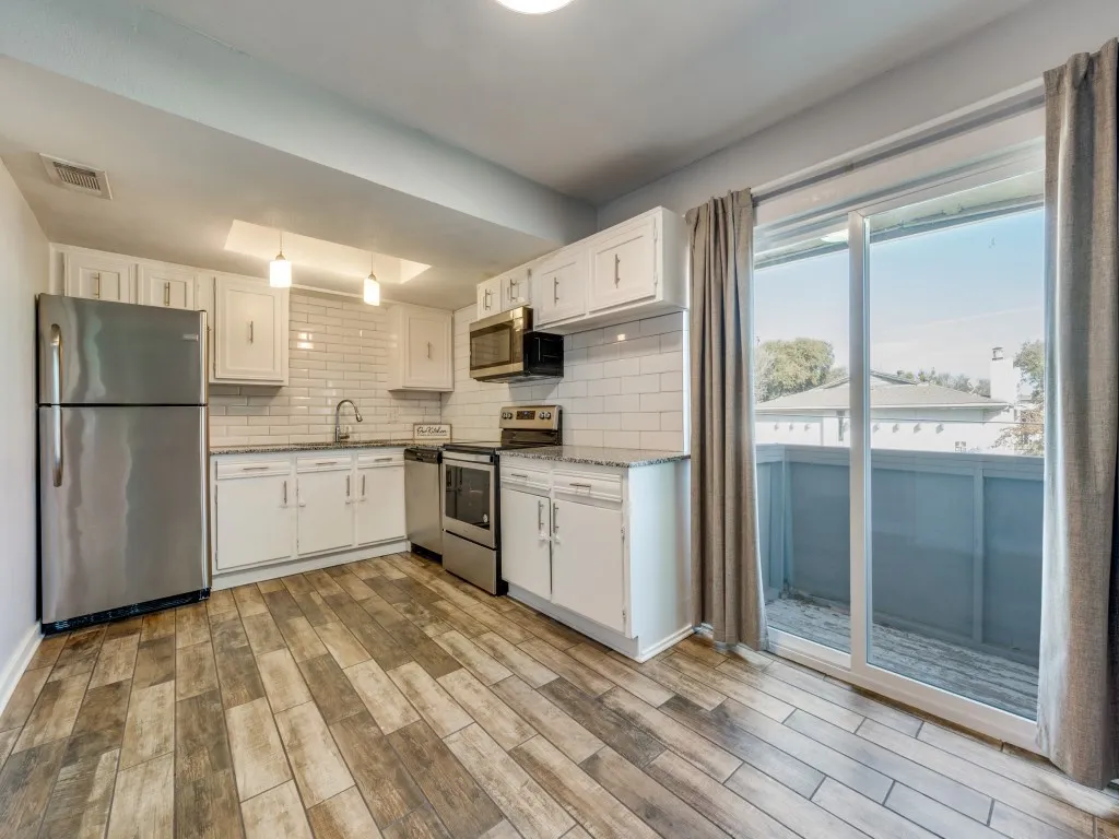 Kitchen featuring wood-finish flooring, white cabinetry, a subway tile backsplash, and stainless steel appliances