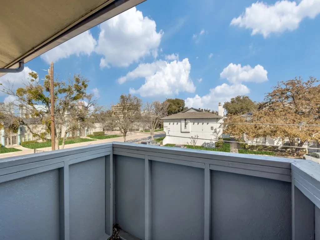 Balcony with painted wood railing overlooking neighborhood foliage and buildings