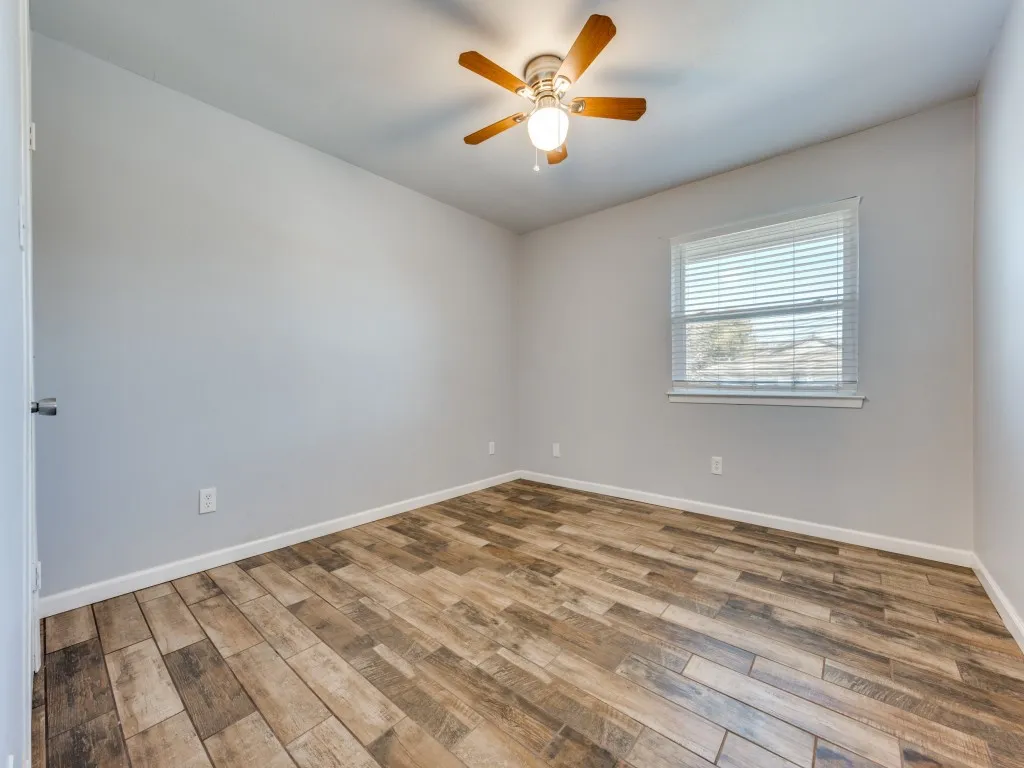 Wood-finish tile flooring, ceiling fan with integrated lighting, and a window with blinds