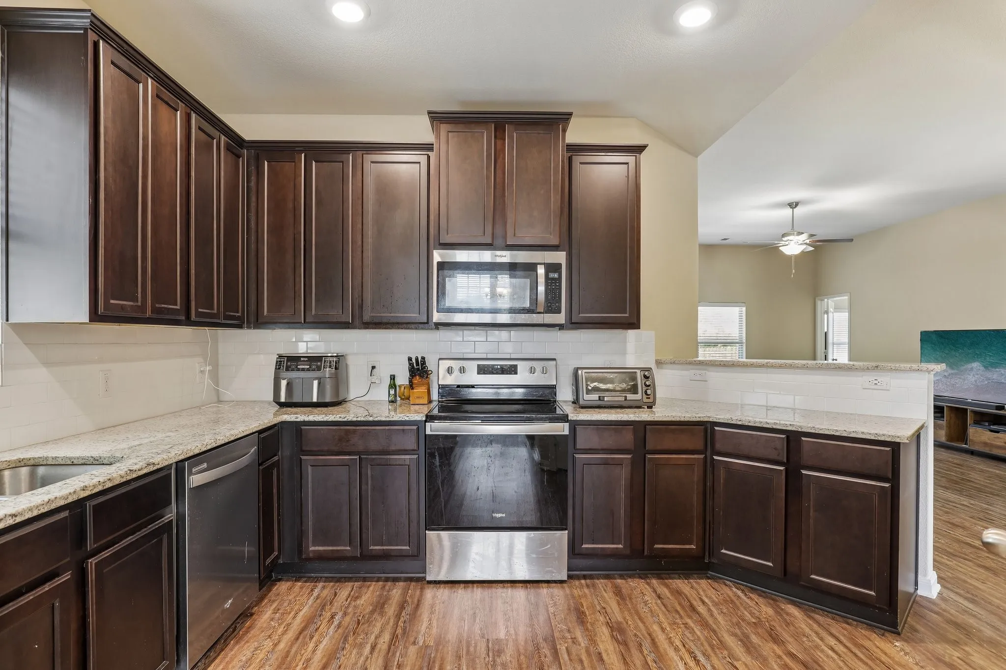 Dark wood cabinetry, stainless steel appliances, granite countertops, subway tile backsplash, and wood-finish flooring